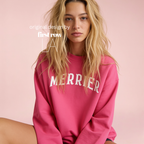 A woman wearing a bright pink crewneck sweatshirt with 'MERRIER' printed in white arched letters across the chest.

Original design and copyright by first row LA, August 11th 2026.