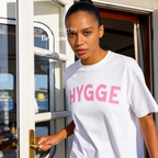 Woman wearing HYGGE T-shirt  with  large pink hand drawn letters.

Original design and copyright by first row LA Aught 18th, 2026.