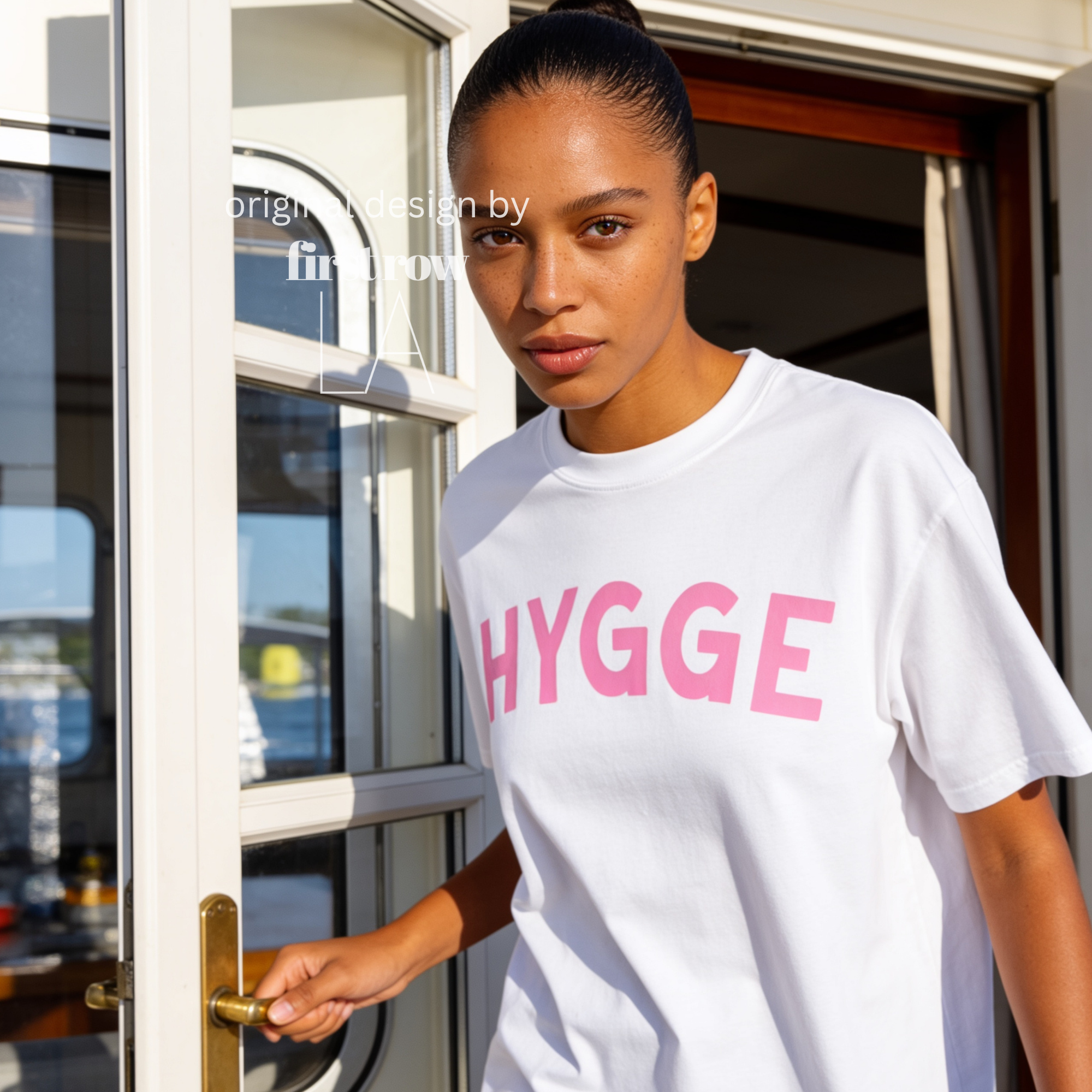 Woman wearing HYGGE T-shirt  with  large pink hand drawn letters.

Original design and copyright by first row LA Aught 18th, 2026.