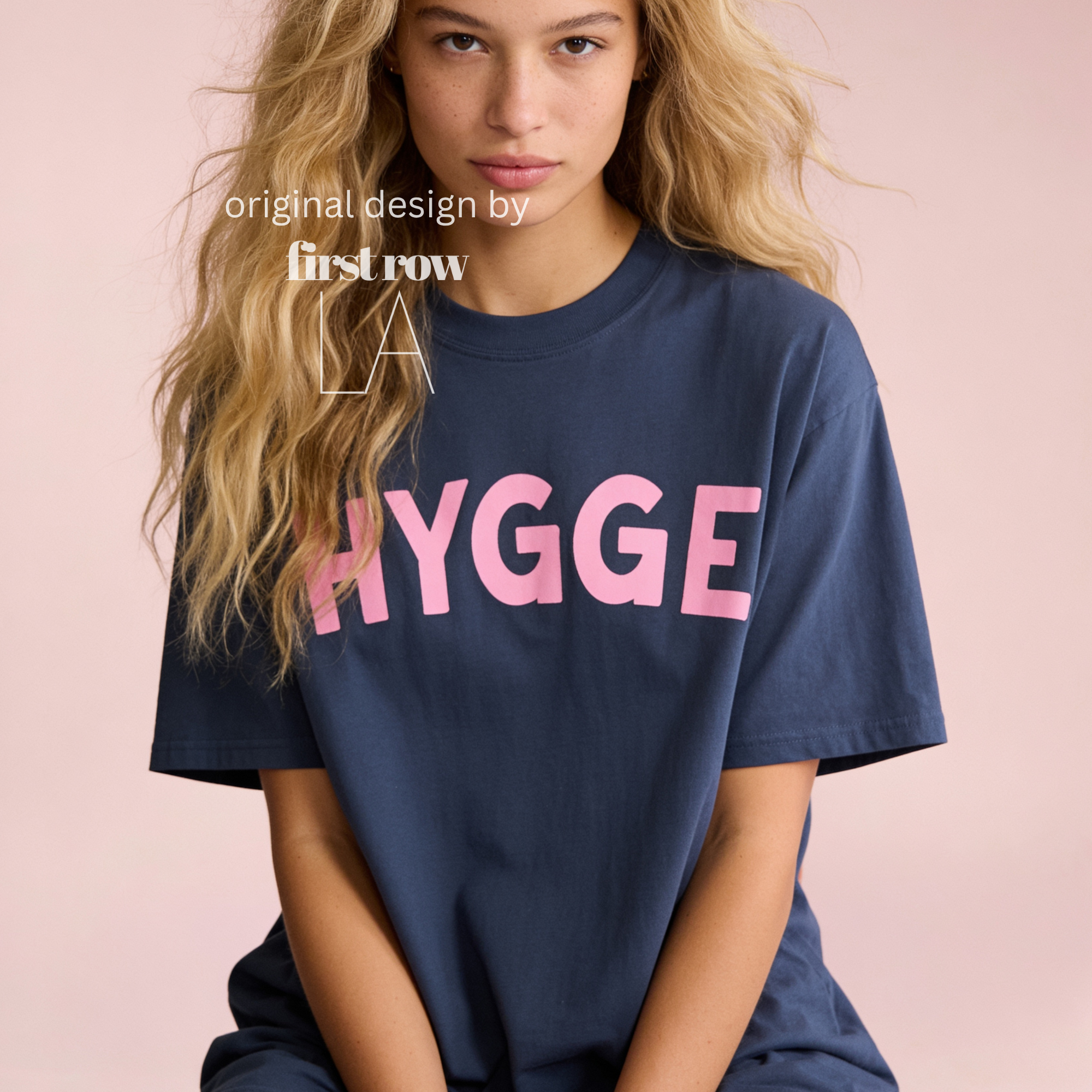 Woman wearing HYGGE T-shirt  with  large pink hand drawn letters.

Original design and copyright by first row LA Aught 18th, 2026.