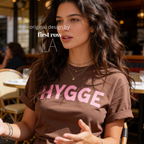Woman wearing HYGGE T-shirt  with  large pink hand drawn letters.

Original design and copyright by first row LA Aught 18th, 2026.