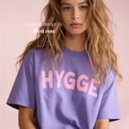 Woman wearing HYGGE T-shirt  with  large pink hand drawn letters.

Original design and copyright by first row LA Aught 18th, 2026.