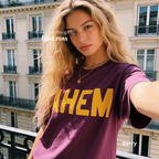 A woman takes a selfie while wearing a plum t-shirt with the word 'AHEM' printed in bold yellow letters across the chest. 

Original design and copyright by first row LA, August 4th 2026.