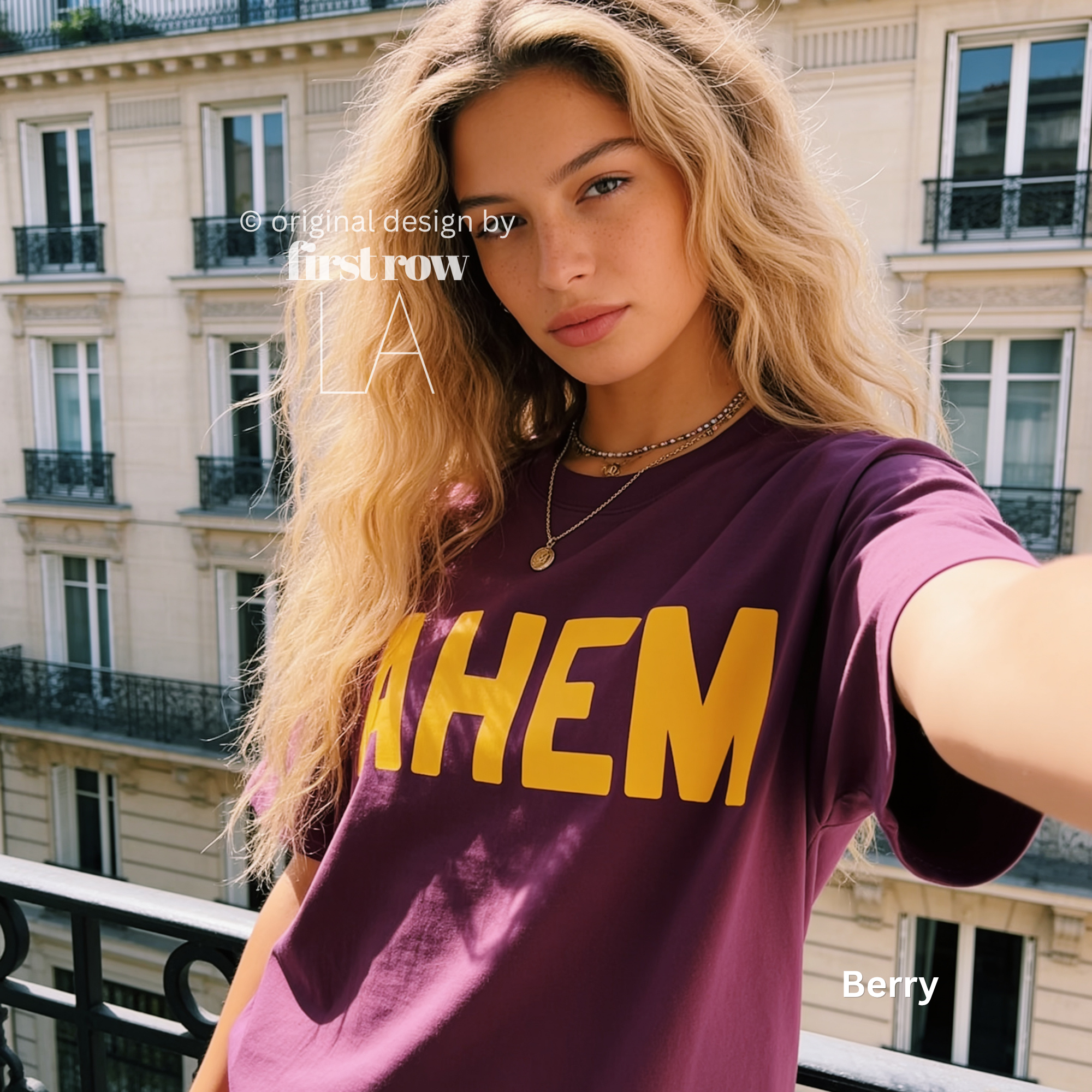 A woman takes a selfie while wearing a plum t-shirt with the word 'AHEM' printed in bold yellow letters across the chest. 

Original design and copyright by first row LA, August 4th 2026.