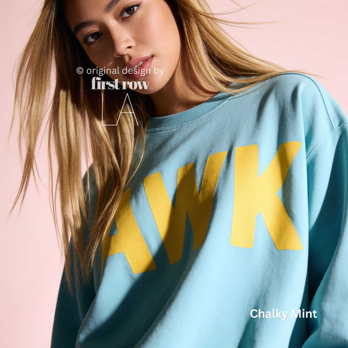 A woman wearing a light blue sweatshirt with large yellow 'AWK' lettering across the front.

Original design and copyright by first row LA, August 4th 2026.