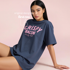 A woman wearing an oversized navy blue t-shirt with pink text reading 'CRISPY BACON Society Club' poses against a solid light pink background. Original design by first row LA.