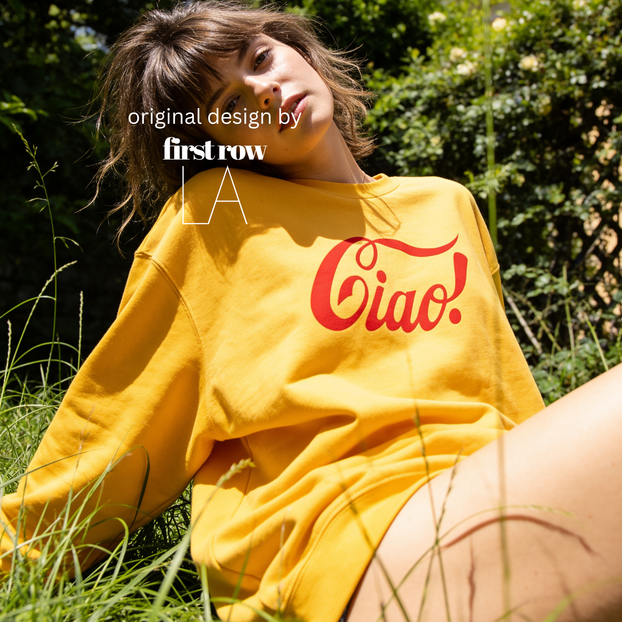 A woman lying in grass outdoors wearing a bright yellow sweatshirt with a large red 'Ciao!' logo across the chest. 

Original design and copyright by first row LA.