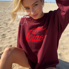 A woman sitting on a sandy beach wearing an oversized maroon sweatshirt with a large red 'Ciao!' graphic across the front. 

Original design and copyright by first row LA.