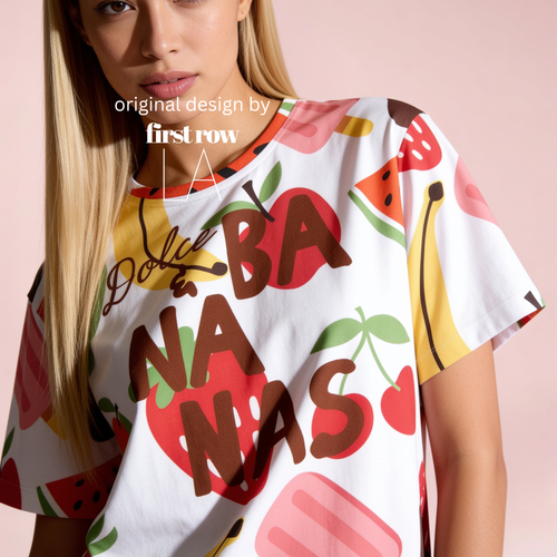 A woman wearing a white short-sleeve T-shirt with a colorful fruit print and large brown text reading 'Dolce and BANANAS' across the front, photographed against a soft pink background. AOriginal design by first row LA.