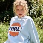 A woman outdoors wearing a light blue sweatshirt with a large retro-style orange, white, and navy 'GIRL' graphic on the front. The image has a watermark overlay reading 'Original designs first row LA'.
