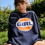 A woman outdoors wearing a navy blue sweatshirt with a large retro-style orange, white, and navy 'GIRL' graphic on the front. The image has a watermark overlay reading 'Original designs first row LA'.