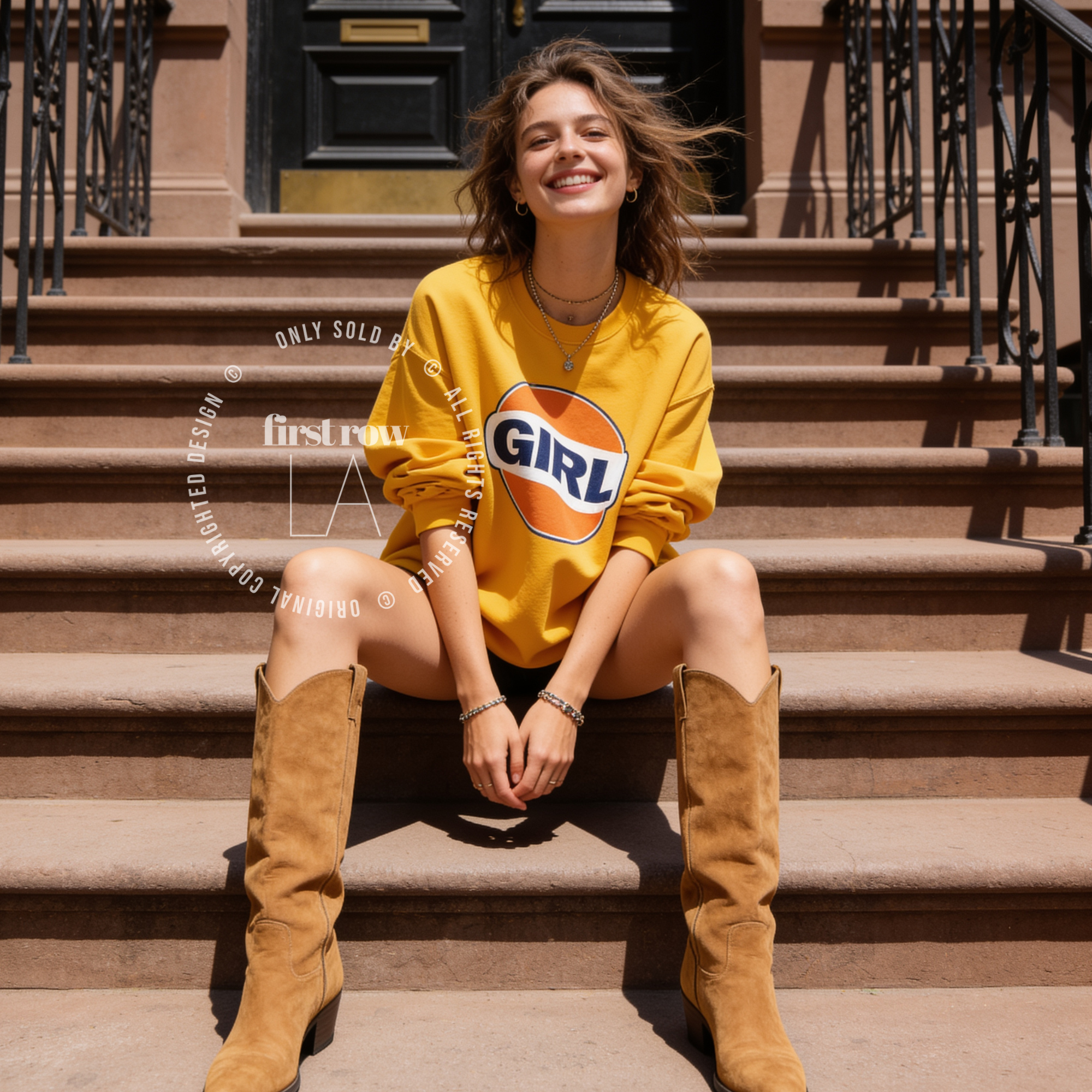 A woman outdoors wearing a gold yellow sweatshirt with a large retro-style orange, white, and navy 'GIRL' graphic on the front. The image has a watermark overlay reading 'Original designs first row LA'.