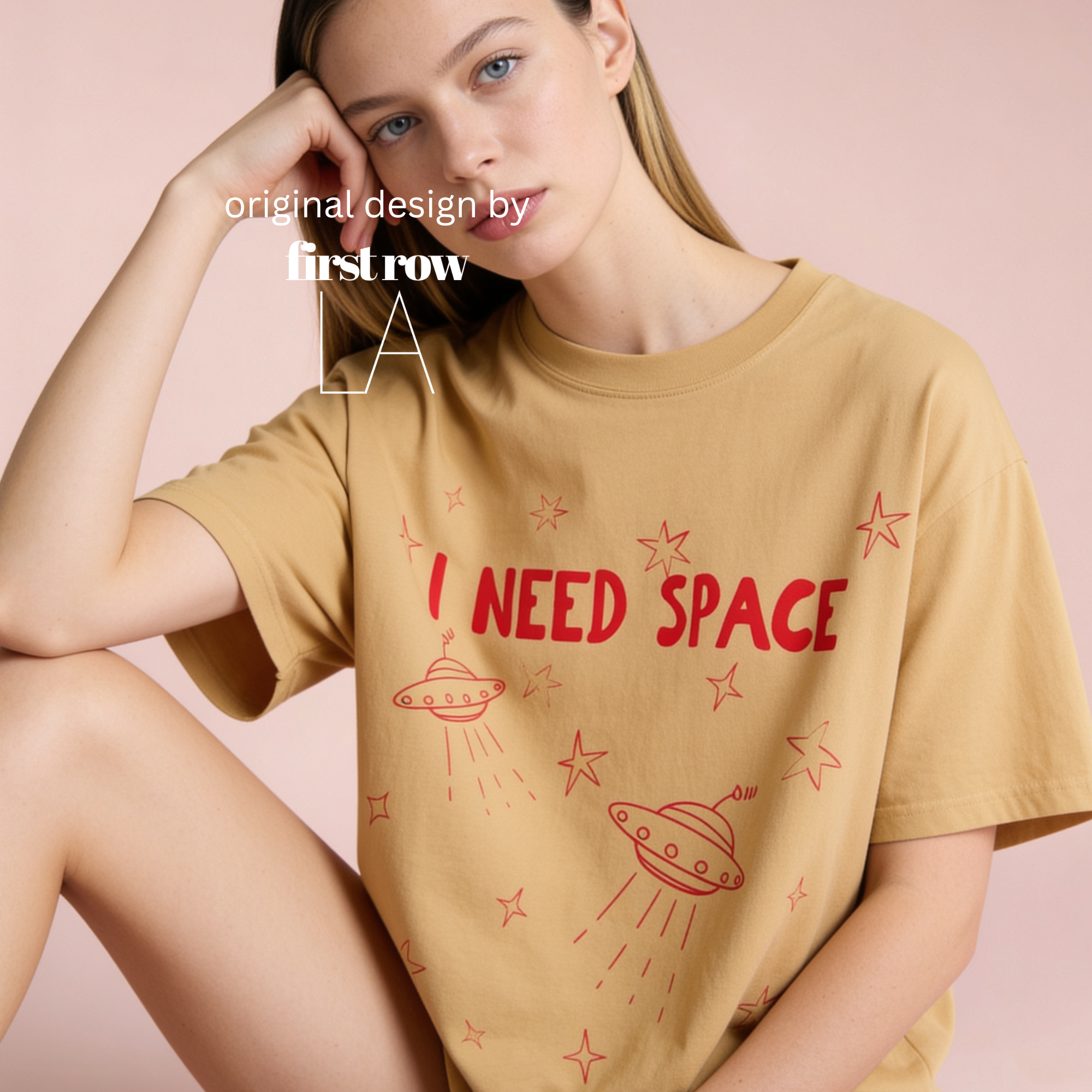A woman wearing a graphic t-shirt with red 'I NEED SPACE' text and space-themed illustrations, posed against a solid pink background. Original design by first row LA.