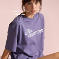 A woman wearing an oversized lavender-purple t-shirt with 'Miss UNDERSTOOD' printed in white across the chest. Original design by first row LA.