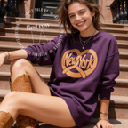 A woman sitting on outdoor stone steps wears a purple sweatshirt with a large gold New York graphic and tan cowboy boots. Original design by first row LA.