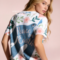 A woman wearing a white short-sleeve t-shirt with a peace dove print, pink flowers, green leaves, and the words 'Peace on Earth' in pink script. 

Original design and copyright by first row LA 2026.
