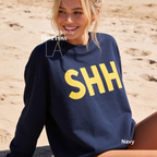 A woman wearing a navy blue sweatshirt with large yellow 'SHH' lettering on the front. 

Original design and copyright by first row LA, August 4th 2026.