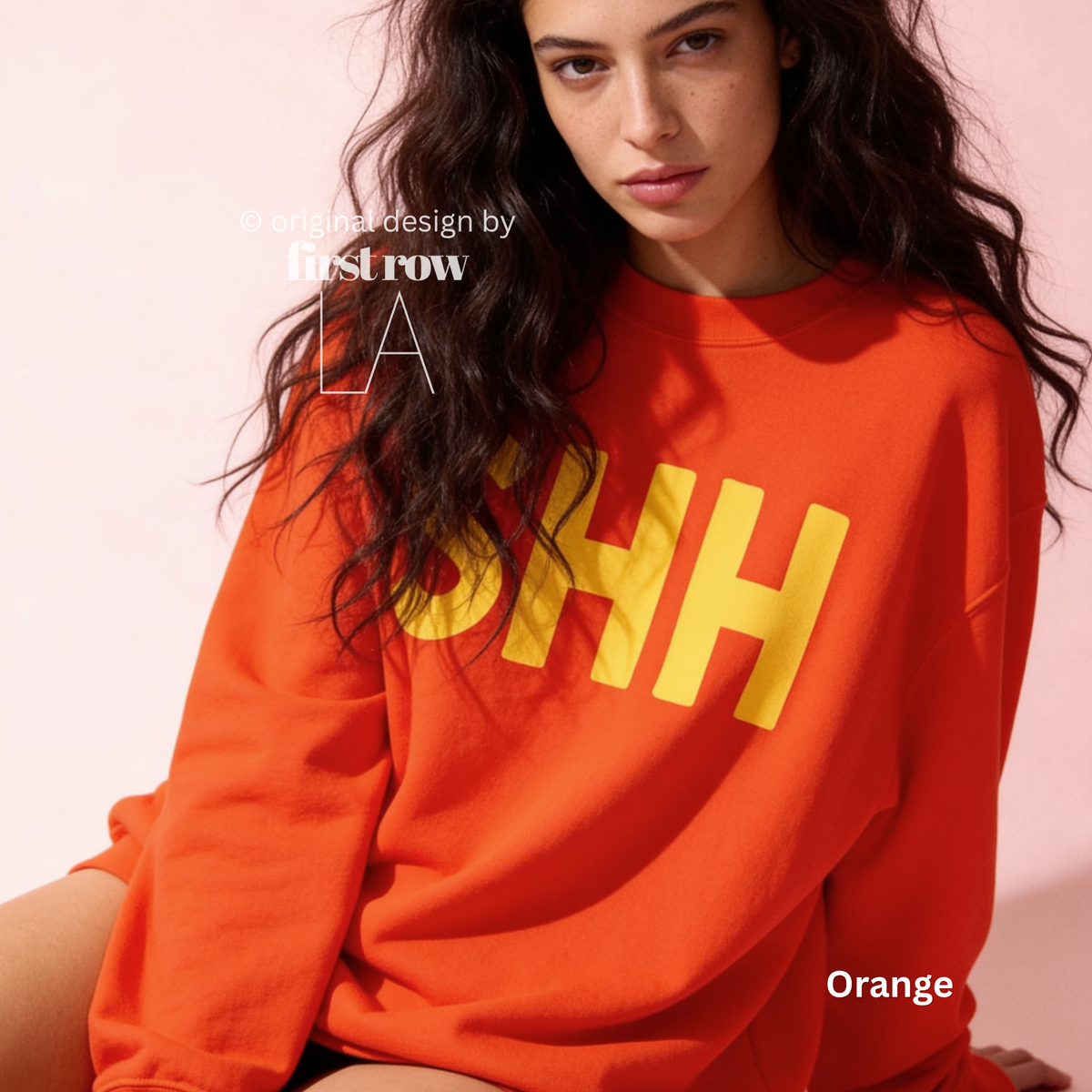 A woman wearing a bright orange sweatshirt with large yellow block letters spelling 'SHH' across the chest.

Original design and copyright by first row LA, August 4th 2026.