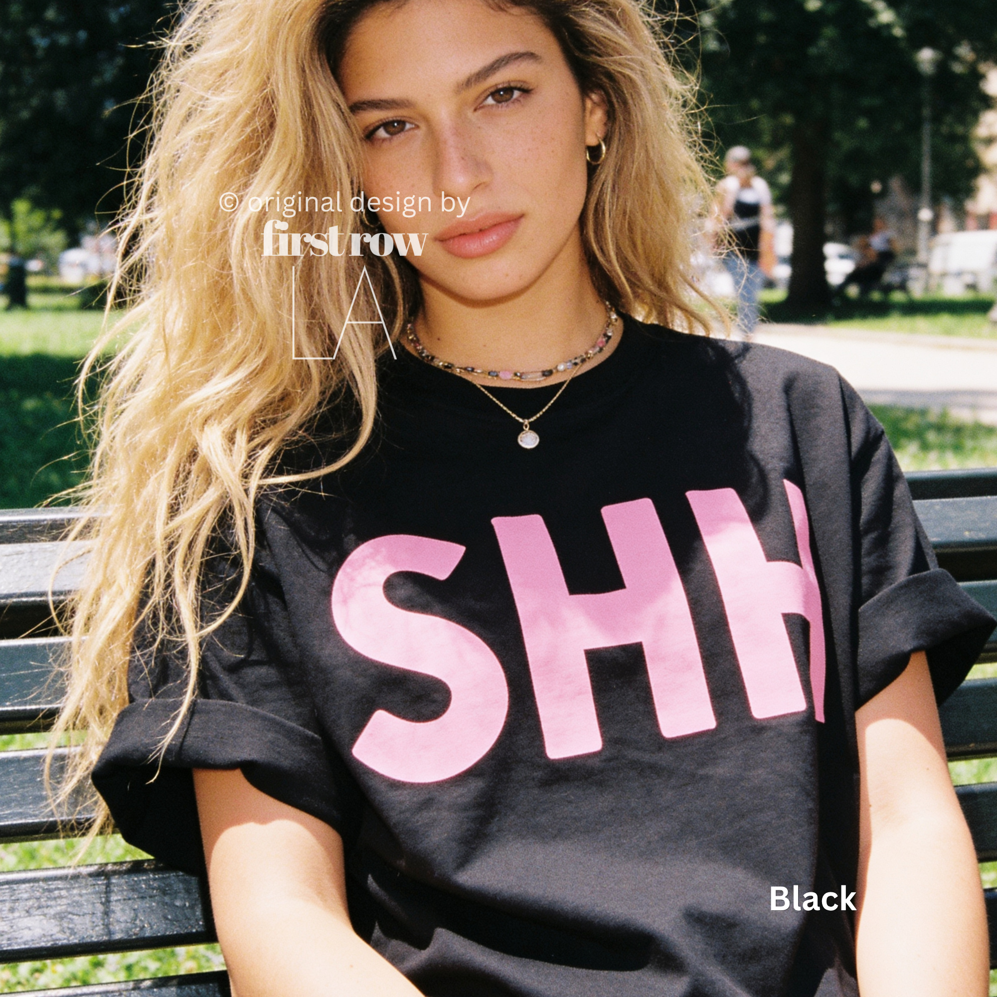 A woman wearing a black T-shirt with large pink letters spelling 'SHH' across the front. 

Original design and copyright by first row LA, August 4th 2026.
