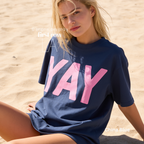 A woman wearing a classic blue t-shirt with pink YAY print.

Original design and copyright by first row LA 2026