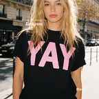 A woman wearing a black t-shirt with pink YAY print.

Original design and copyright by first row LA 2026