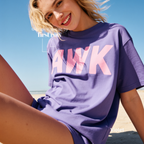 A woman sitting on a beach wearing a violet purple oversized t-shirt with a pink 'AWK' graphic on the front.

Original design and copyright by first row LA, August 4th 2026.