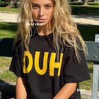 A woman wearing a black black T-shirt with the word 'DUH' printed in bold yellow letters across the front. 

Original design and copyright by first row LA, August 4th 2026.