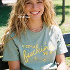 Woman wearing 'C'est la fucking vie' T-shirt with small yellow star accents. 

Original design and copyright by first row LA, August 4th 2026.