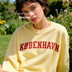 A woman wearing a pale yellow sweatshirt with 'KØBENHAVN' printed across the chest in dark red collegiate lettering, 

Copenhagen shirt.

Original design and copyright by first row LA.