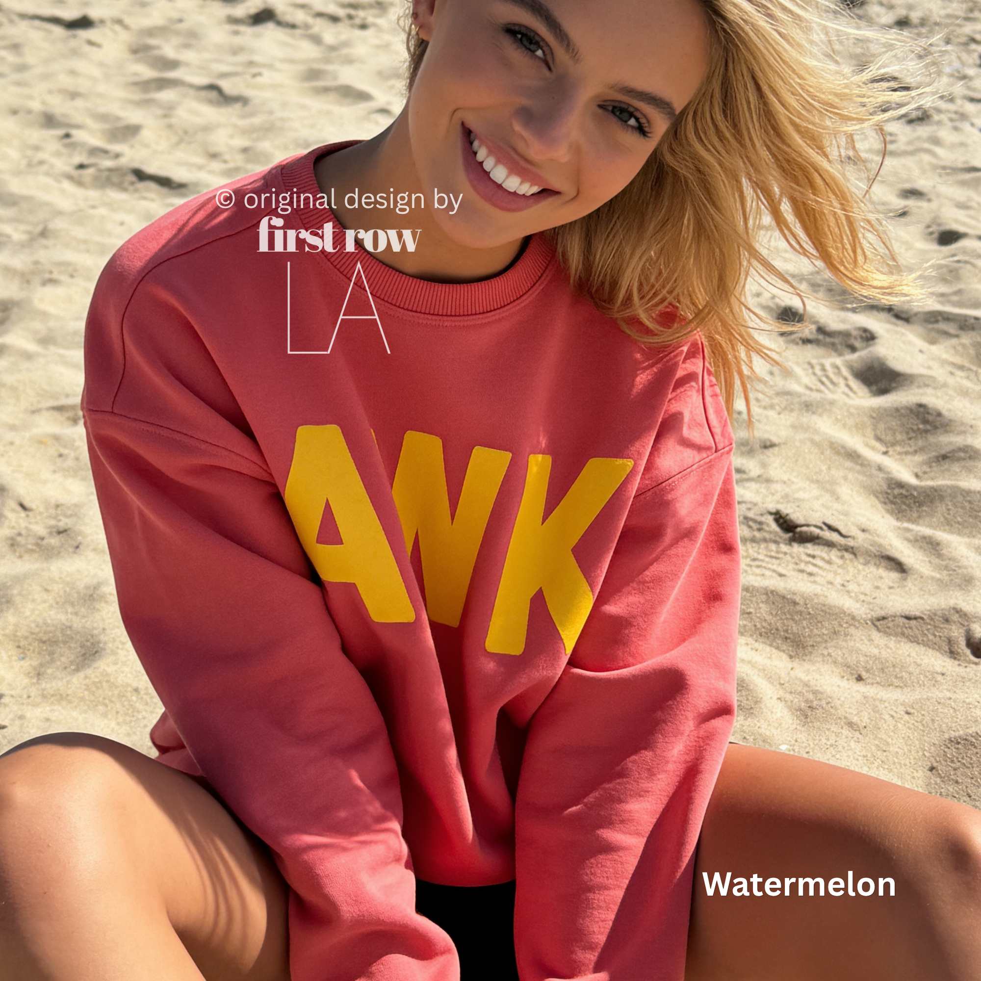A woman sitting on a sandy beach wearing a coral pink sweatshirt with large yellow block letters spelling 'AWK' across the front. 

Original design and copyright by first row LA, August 4th 2026.