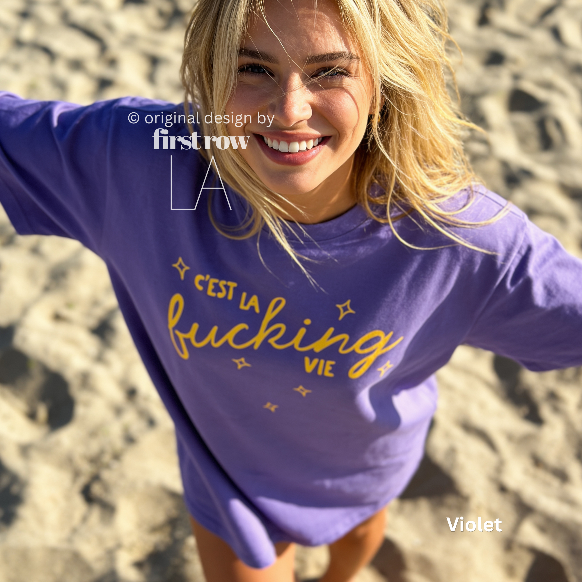 Woman wearing 'C'est la fucking vie' T-shirt with small yellow star accents. 

Original design and copyright by first row LA, August 4th 2026.