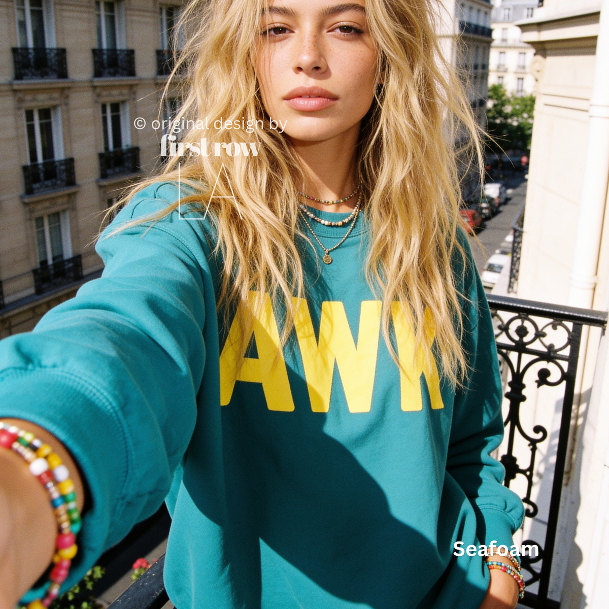 A woman takes a selfie in Paris while wearing a teal sweatshirt with large yellow 'AWK' lettering on the front. 

Original design and copyright by first row LA, August 4th 2026.