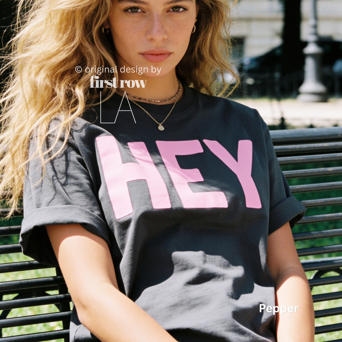 A woman wearing dark grey T-shirt with pink 'HEY' print.

Original design and copyright by first row LA 2026.