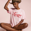 A woman wearing a light pink graphic T-shirt with red 'Karma COWGIRL' lettering and a brown cowboy hat.

Original design and copyright by first row LA.