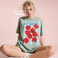 A woman wearing an oversized sage green graphic Les Tomates T-shirt with a red tomato print and blue lettering.

Original design and copyright by first row LA 2025.