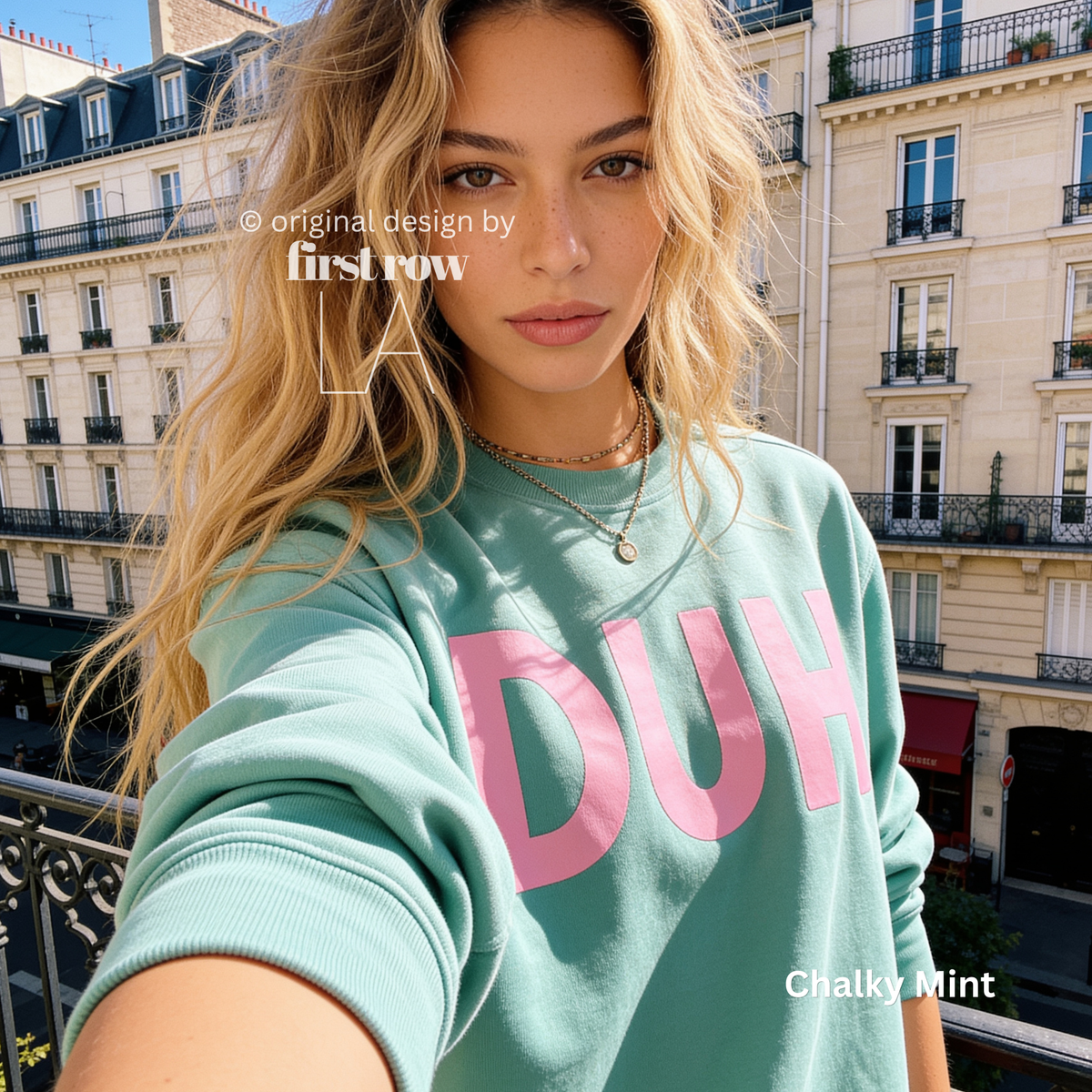 A woman in Paris wearing a mint green sweatshirt with the word 'DUH' printed in pink across the front. 

Original design and copyright by first row LA, August 4th 2026.