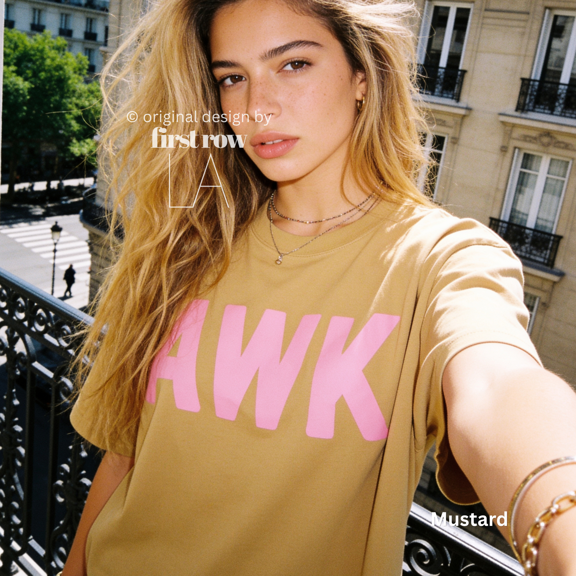 A woman takes a selfie while wearing a mustard yellow t-shirt with the word 'AWK' printed in bold pink letters across the chest. 

Original design and copyright by first row LA, August 4th 2026.