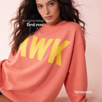 A woman wearing a terracotta-colored oversized sweatshirt with large yellow 'AWK' lettering across the chest.

Original design and copyright by first row LA, August 4th 2026.