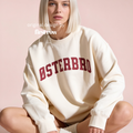 A woman wearing a cream-colored crewneck sweatshirt with 'ØSTERBRO' printed in dark red across the chest.

Original design and copyright by first row LA.