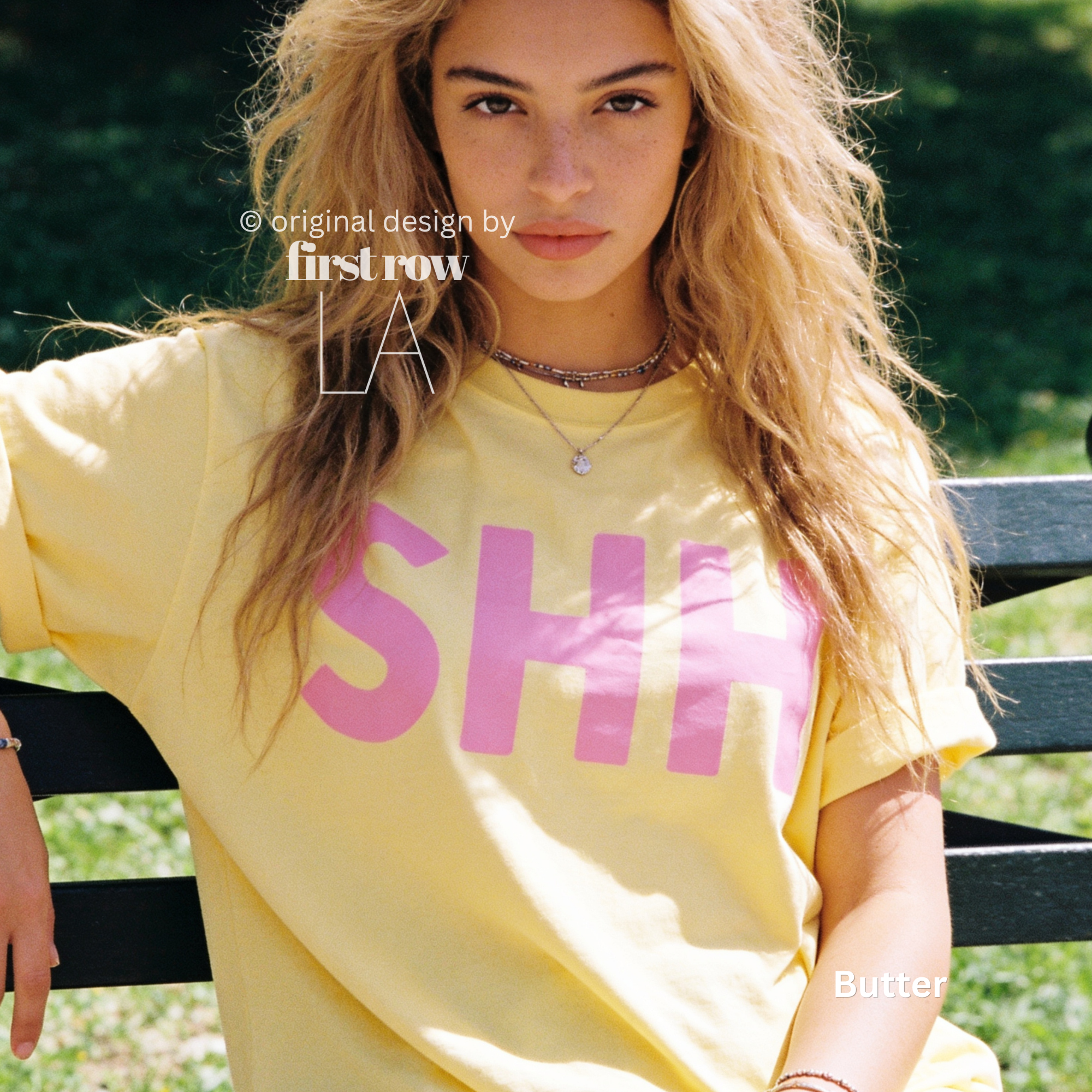 A woman wearing a pale yellow oversized T-shirt with large pink block letters spelling 'SHHH'. 

Original design and copyright by first row LA, August 4th 2026.