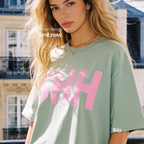 A woman wearing a sage green t-shirt with a bold pink 'SHH' graphic on the front.
Original design and copyright by first row LA, August 4th 2026.
