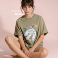A woman sits wearing an oversized olive green T-shirt with a large front graphic of a white dove, flowers, and the words 'Peace on Earth.' 

Original design by first row LA.