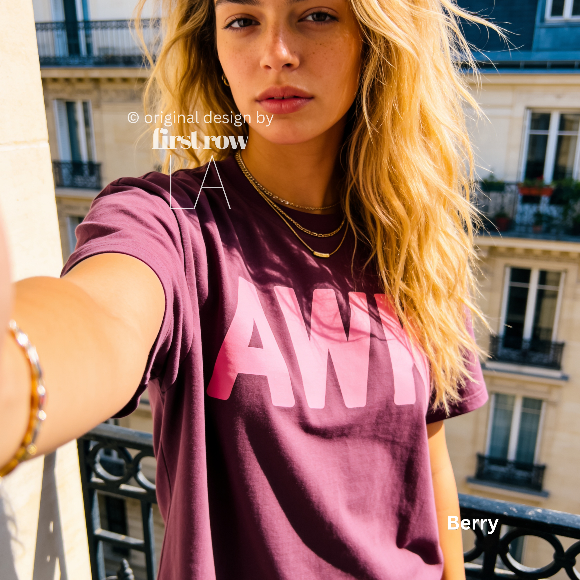 A woman takes a selfie on a balcony in Paris, while wearing a berry purple t-shirt with a large pink graphic text 'AWK' on the front. 

Original design and copyright by first row LA, August 4th 2026.