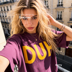 A woman wearing a berry purple oversized t-shirt with a bold yellow 'DUH' graphic on the front. 

Original design and copyright by first row LA, August 4th 2026.