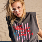 A woman wearing a sleeveless cream-colored t-shirt with a graphic print that reads 'POUR YOURSELF A CUP OF AMBITION' in red, decorated with pink vertical stripes, a blue moka pot, and a small coffee cup. 

Original design and copyright by first row LA.