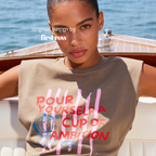 A woman wearing a sleeveless cream-colored t-shirt with a graphic print that reads 'POUR YOURSELF A CUP OF AMBITION' in red, decorated with pink vertical stripes, a blue moka pot, and a small coffee cup. 

Original design and copyright by first row LA.