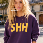 A woman wearing a purple crewneck sweatshirt with large yellow 'SHH' lettering on the front.

Original design and copyright by first row LA, August 4th 2026.