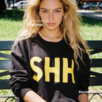 A woman wearing a black crewneck sweatshirt with large yellow 'SHH' lettering on the front. 

Original design and copyright by first row LA, August 4th 2026.