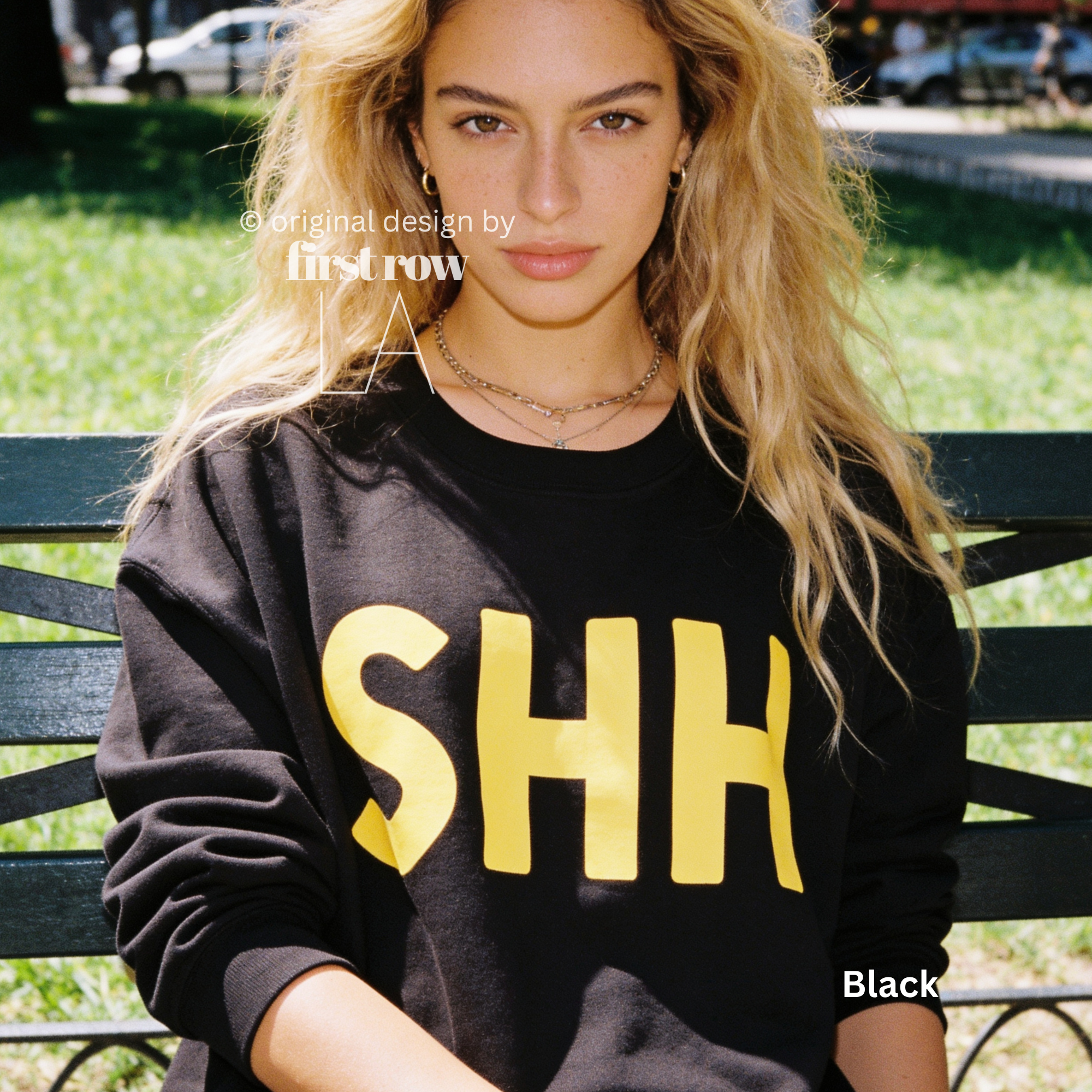 A woman wearing a black crewneck sweatshirt with large yellow 'SHH' lettering on the front. 

Original design and copyright by first row LA, August 4th 2026.