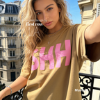 A woman wearing a T-shirt with large pink 'SHH' lettering on the front, photographed on a balcony in Paris.

Original design and copyright by first row LA, August 4th 2026.